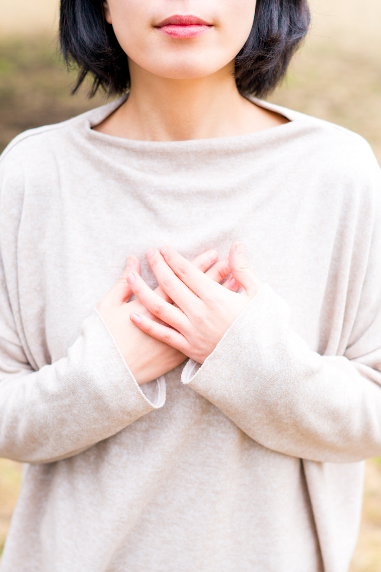 Woman wearing a cream sweater with her hands crossed on her heart